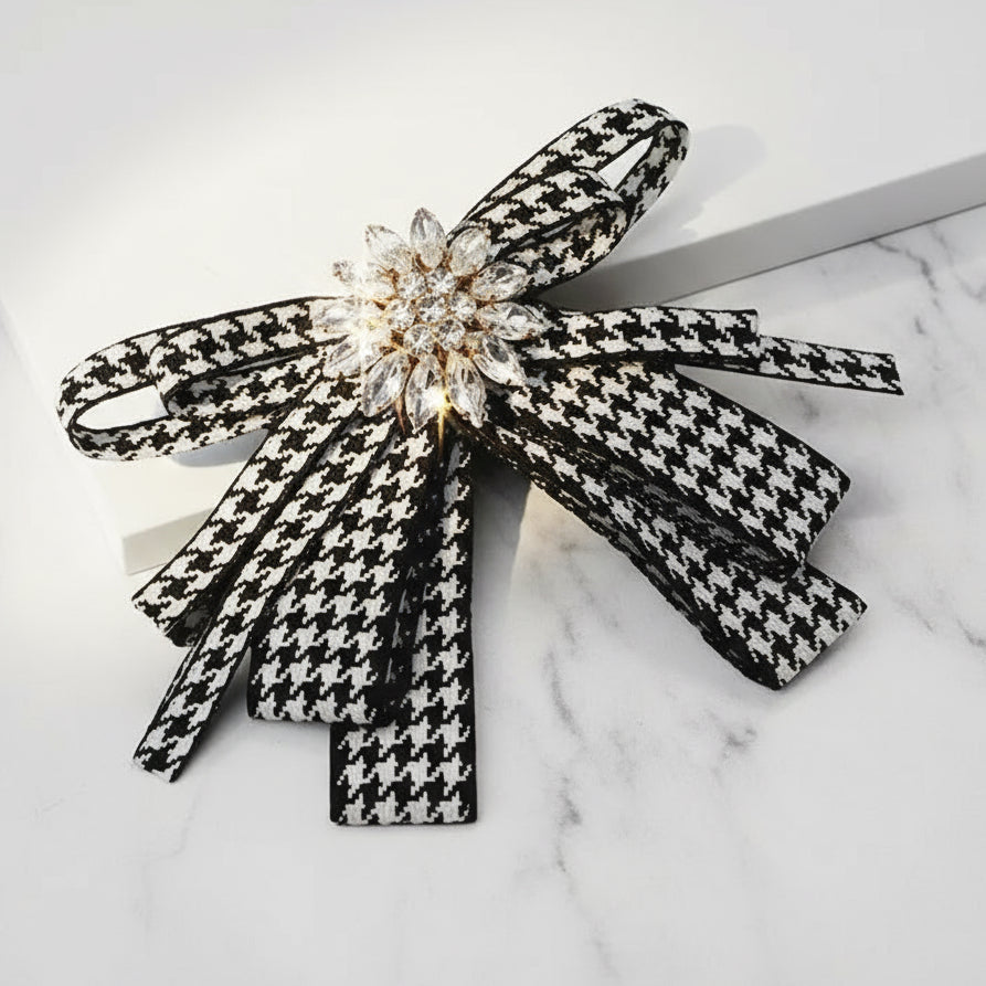Black and white houndstooth bow hair clip with decorative center on a light gray background