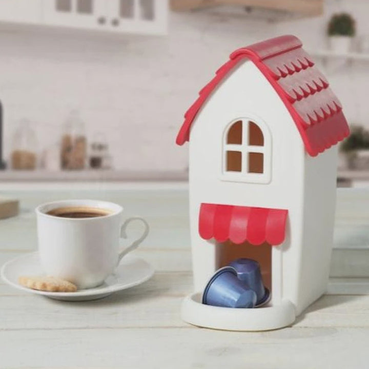House-shaped coffee pod holder with a cup of coffee and cookies on a kitchen counter.