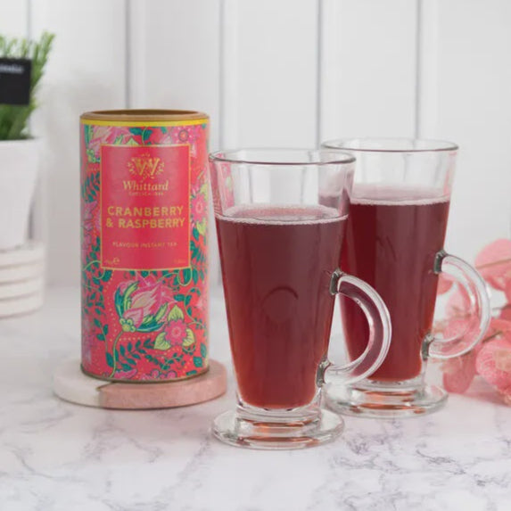 Two glasses of cranberry raspberry tea with a canister on a marble surface.