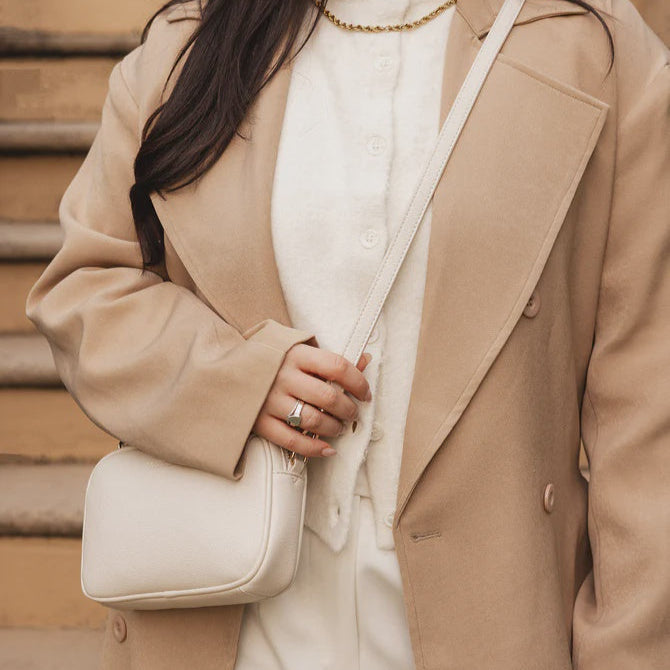 Person wearing a beige coat and white sweater, holding a beige handbag on wooden steps.
