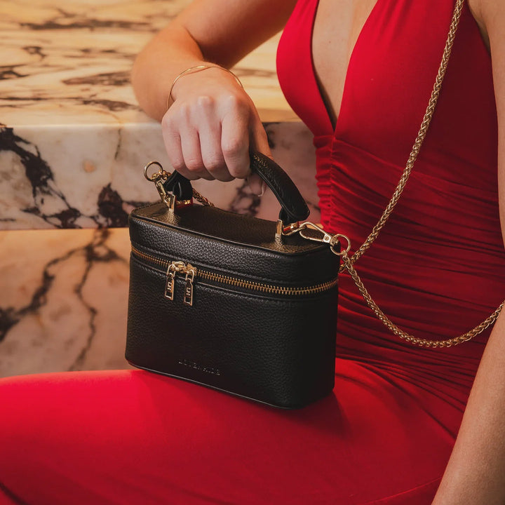 Person in a red dress holding a black louenhide ladies handbag with a gold chain strap.