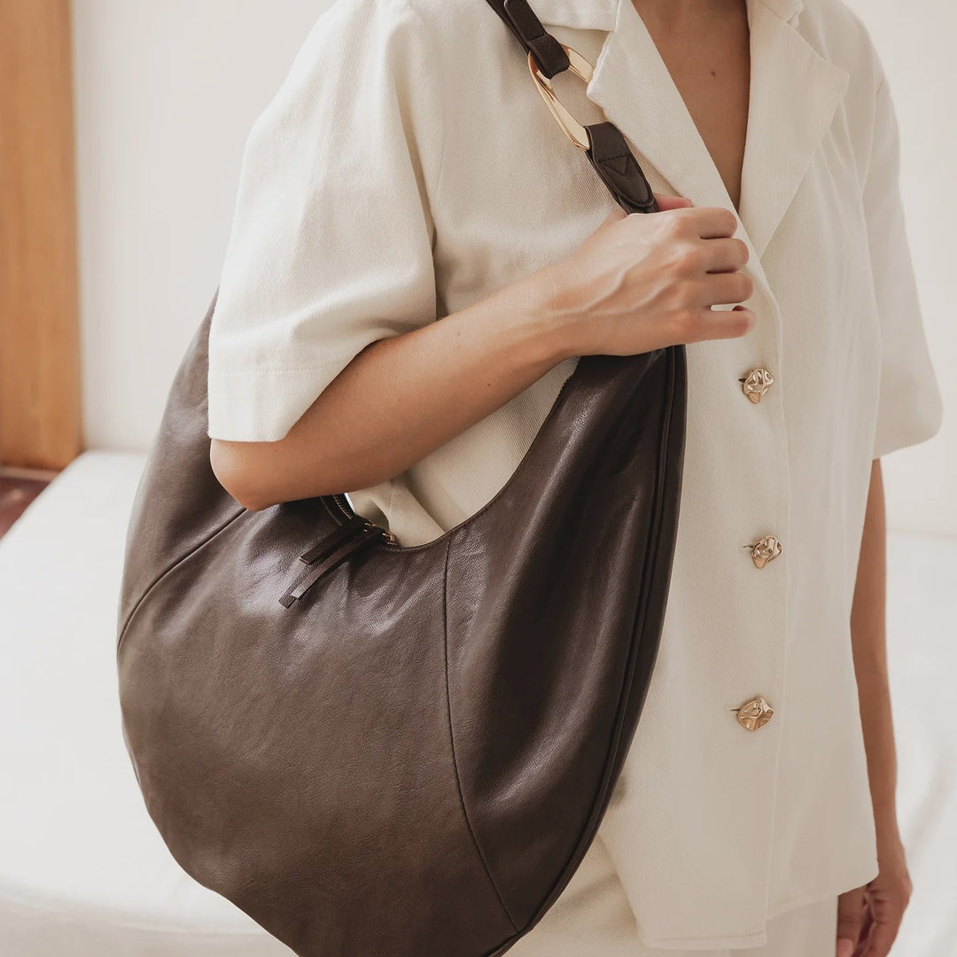 Person holding a brown louenhide bag wearing a white outfit with gold buttons.