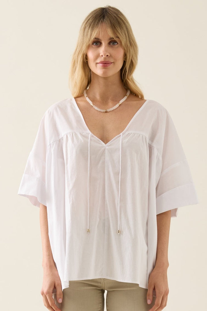 Woman wearing a white blouse and beige pants on a plain background