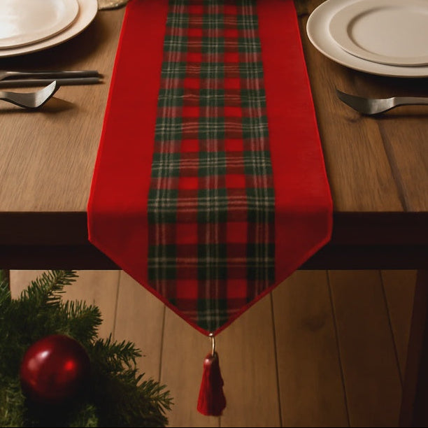 Decorative Christmas table setting with a red plaid runner, candles, and ornaments on a wooden table.