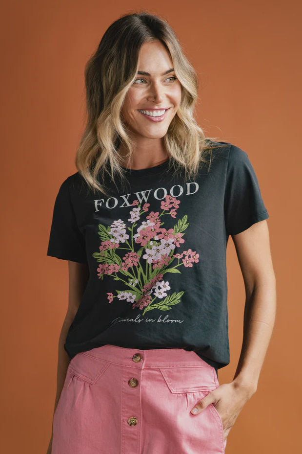 Woman wearing a black t-shirt with floral design and 'FOXWOOD' text on an orange background