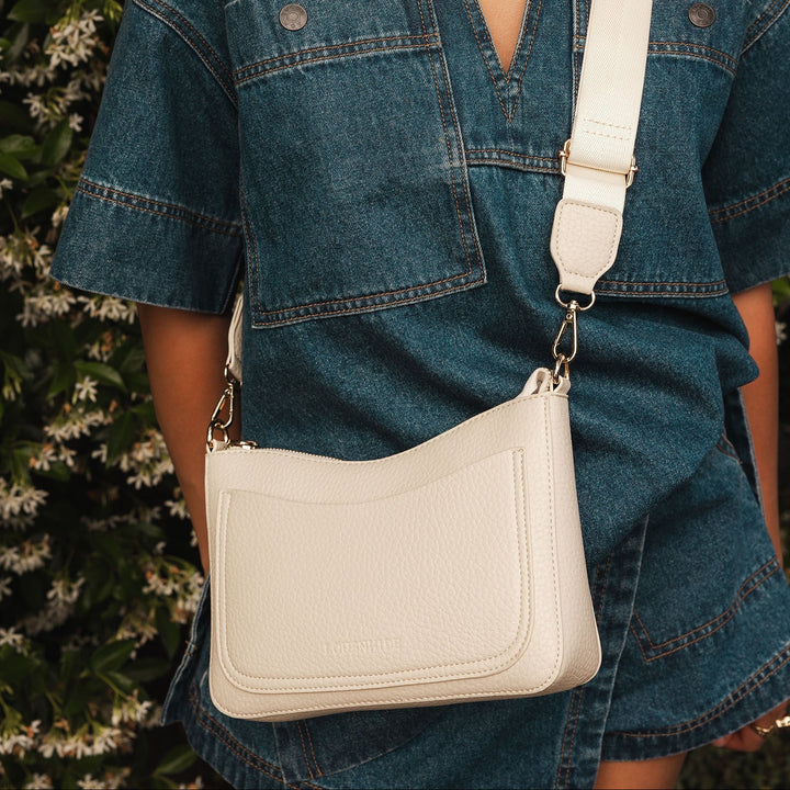 Person wearing a blue denim dress with a beige crossbody bag against a blurred natural background