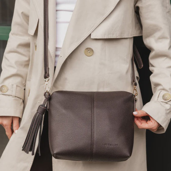 Person wearing a beige trench coat holding a dark brown leather bag.