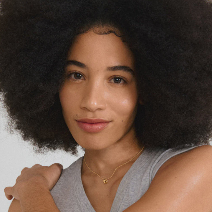 Woman with an afro hairstyle wearing a gray sleeveless top against a plain background