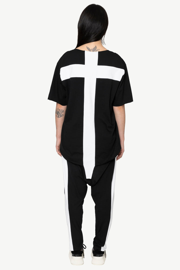 Person wearing a black outfit with a large white cross on the back against a white background