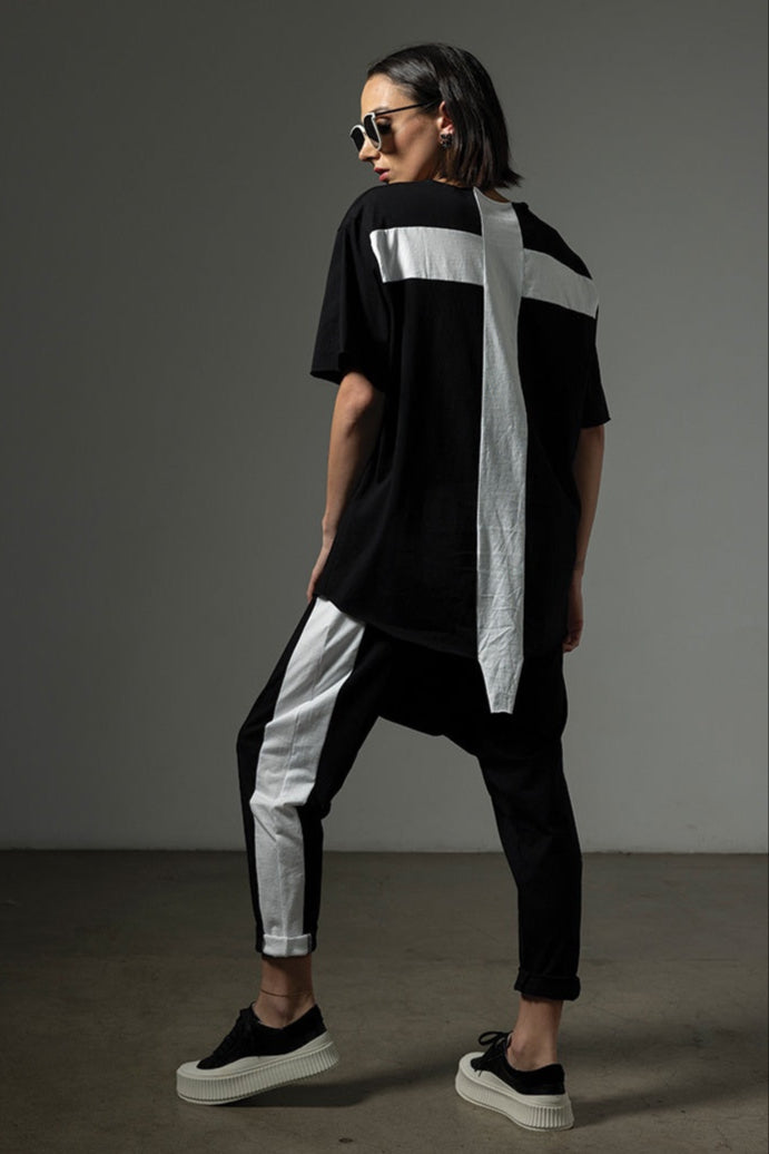 Person wearing a black and white outfit with sunglasses against a gray background