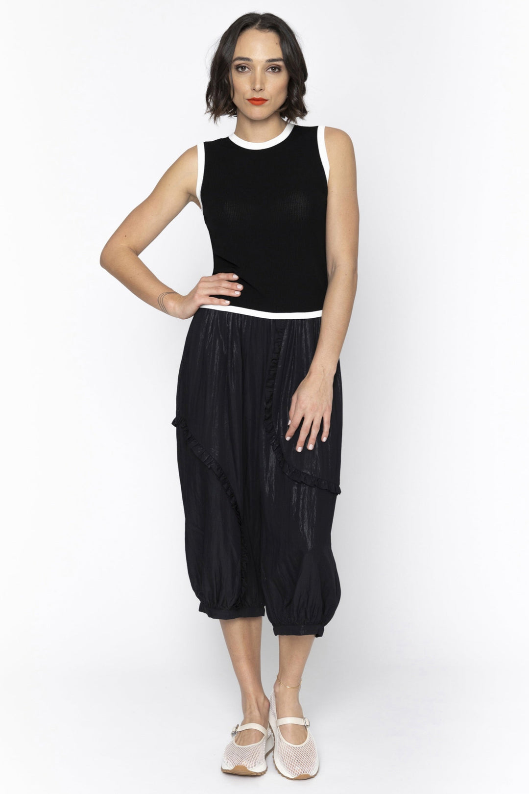 Woman wearing a black sleeveless top and black harem pants on a white background
