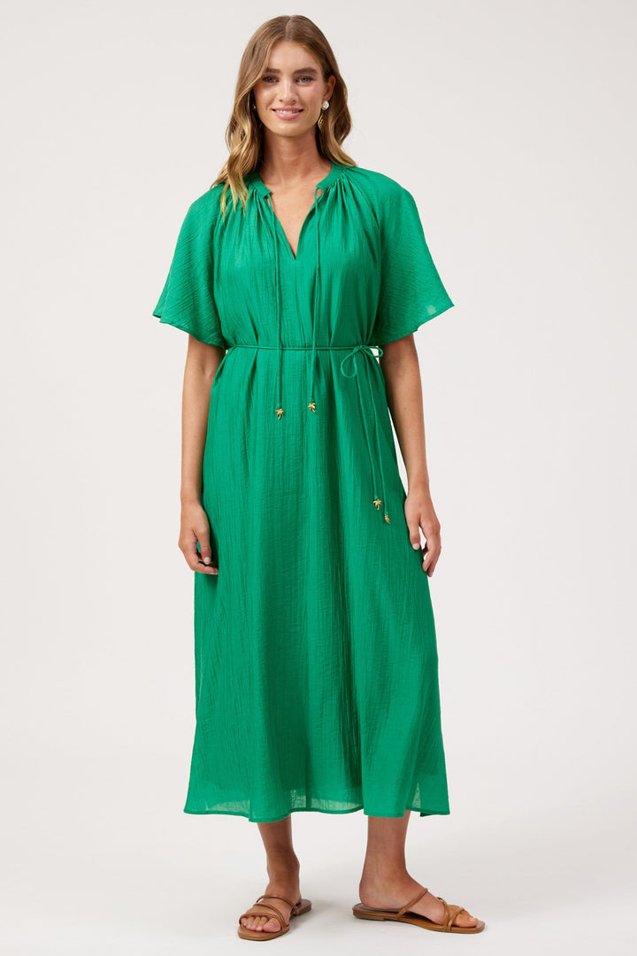 A woman modeling a bright green midi dress with short flutter sleeves, a V-neckline, and a drawstring waist, photographed against a plain light gray studio background.