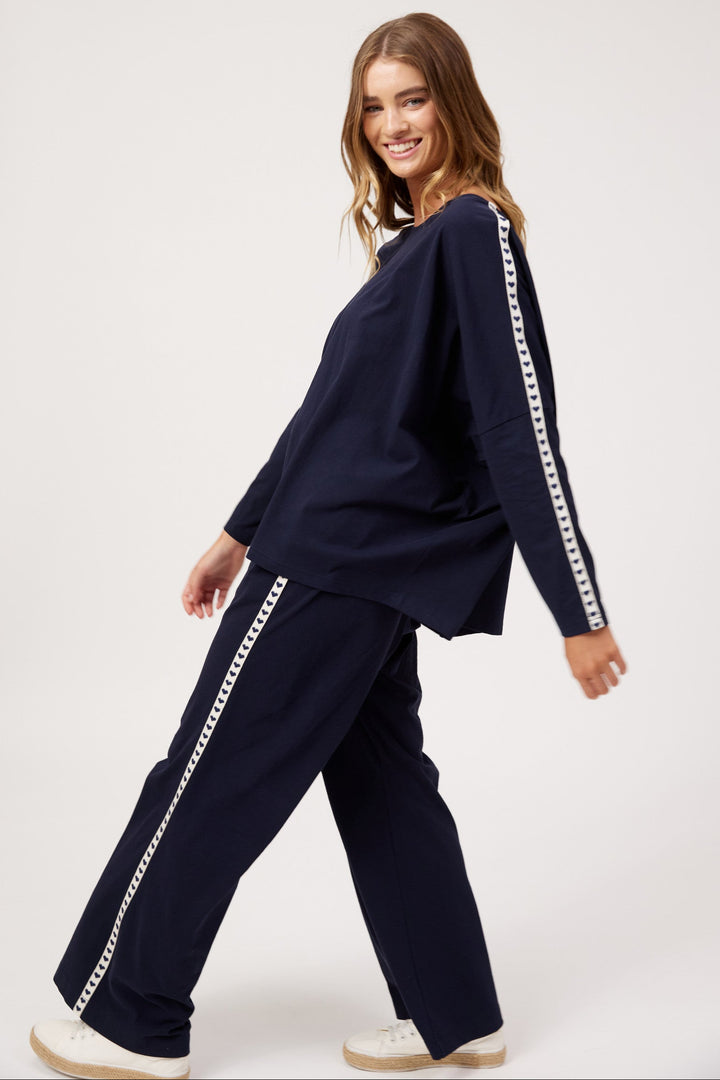 A woman modeling a matching navy blue lounge set with white chain-link trim down the sleeves and pants, posed against a clean white studio background.