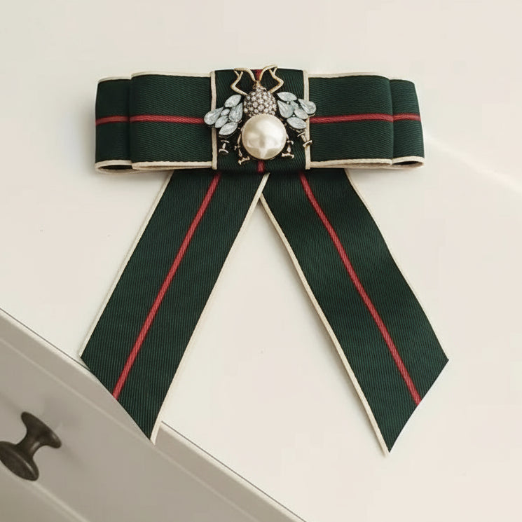 Decorative brooch with green ribbons and a central gemstone on a light background