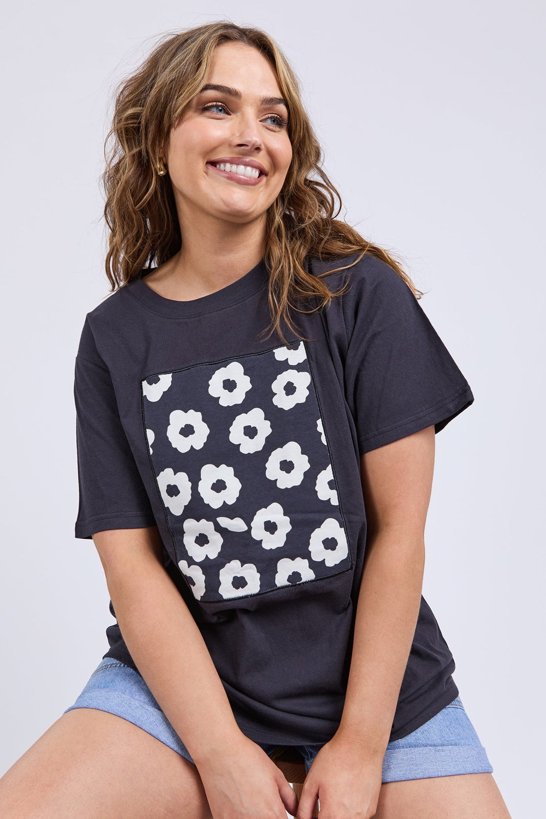 Woman wearing a black t-shirt with white floral pattern and light blue shorts on a plain background