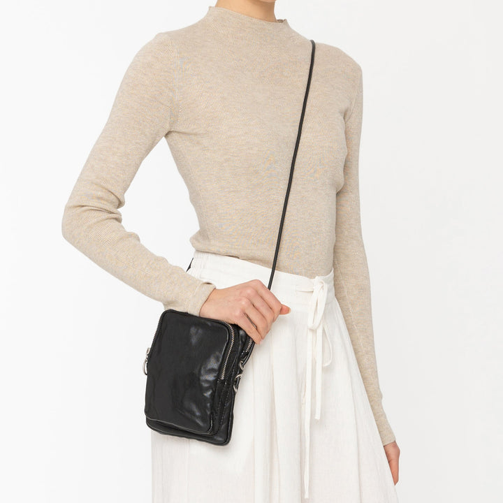 Woman wearing a beige top and white pants with a black handbag on a white background
