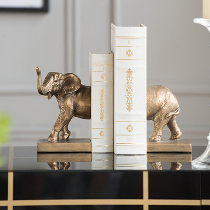 Bronze elephant bookends on a shelf with decorative books.
