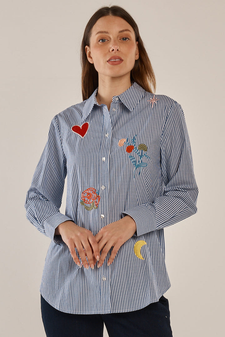 Woman wearing a blue striped shirt with floral and heart designs on a plain background