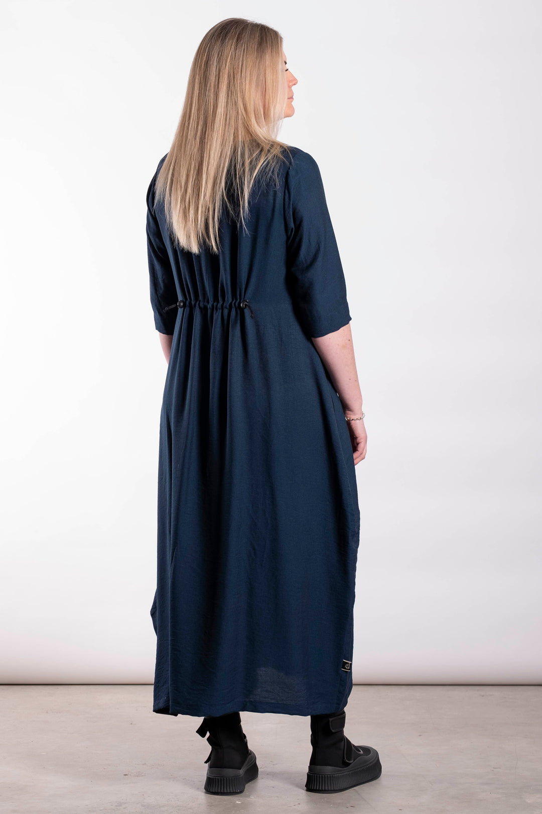 Woman wearing a long navy dress standing against a white background