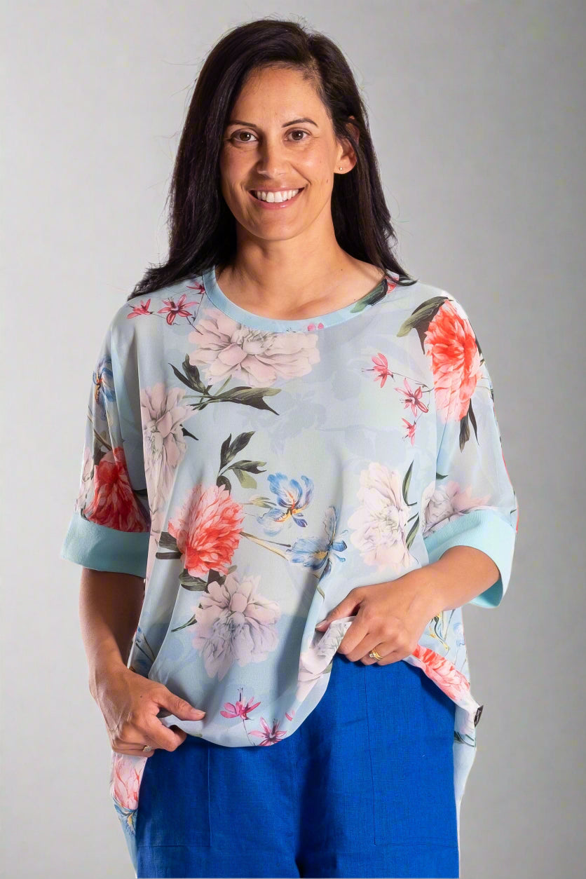 Woman wearing a floral top and blue pants on a white background