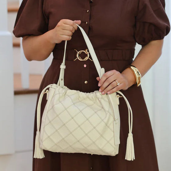 Woman in a brown dress holding a white quilted handbag indoors.