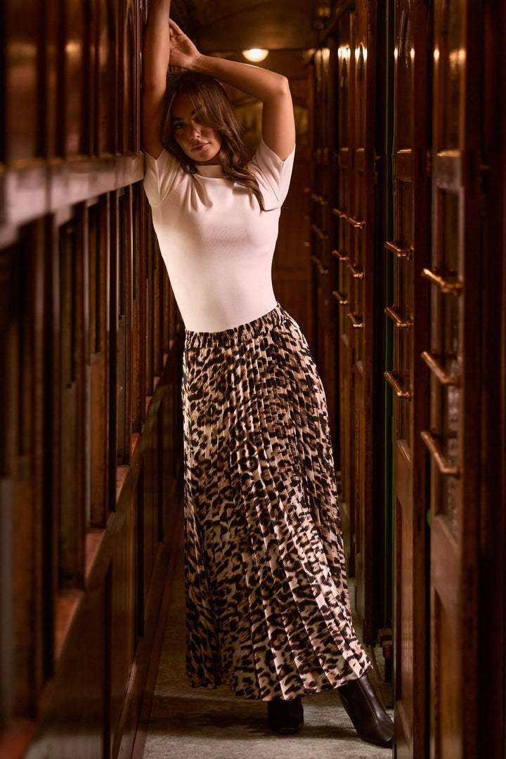 Woman in a leopard print skirt standing in a dimly lit hallway with wooden panels.
