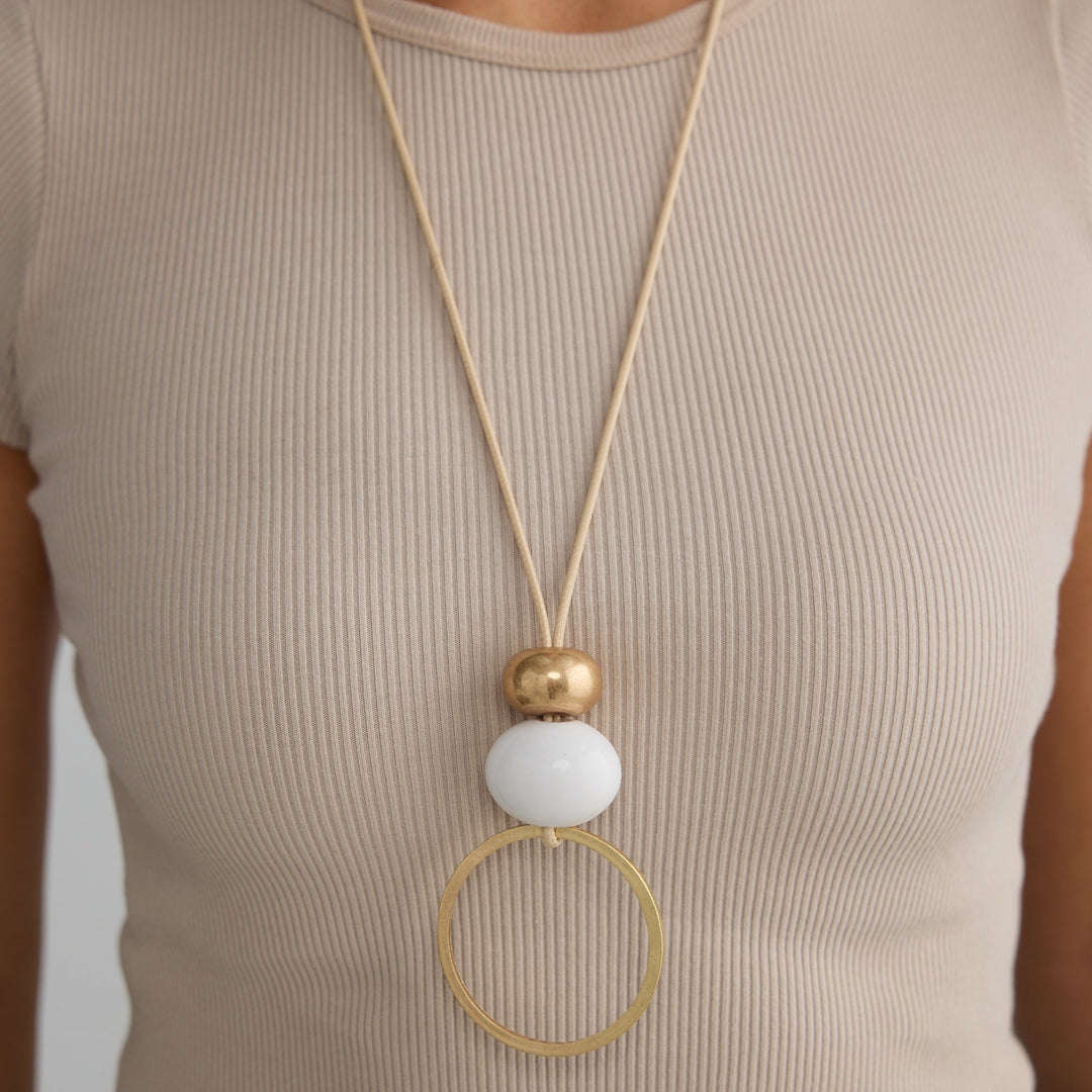 Long necklace with a white pendant and gold accents worn by a person in a beige top.