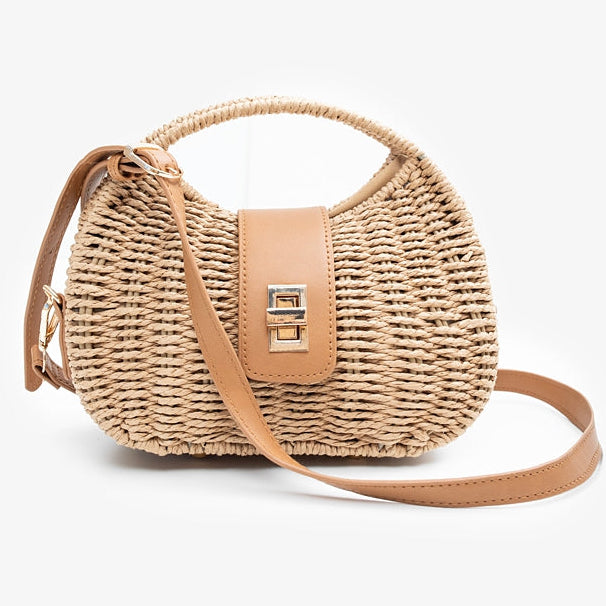 A small woven straw handbag with a tan leather top handle and flap closure, featuring a gold-tone metal clasp and a matching tan shoulder strap, set against a plain light gray background.