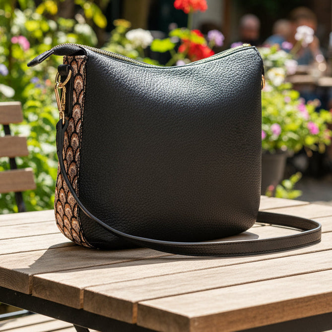 Black handbag with a decorative patterned strap on a white background