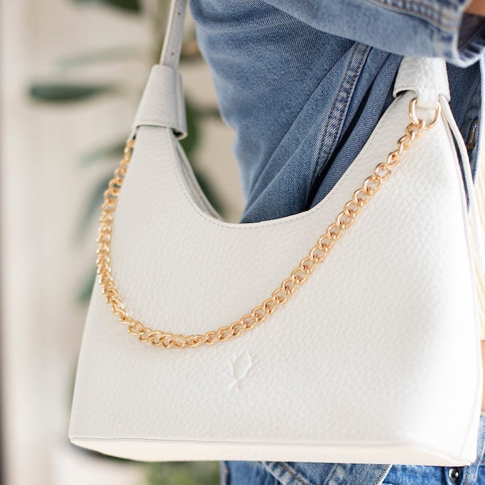 White handbag with gold chain strap held by a person wearing blue jeans.