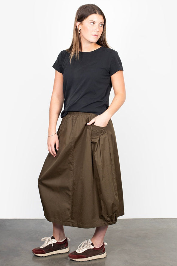 Woman wearing a black t-shirt and brown skirt on a plain background