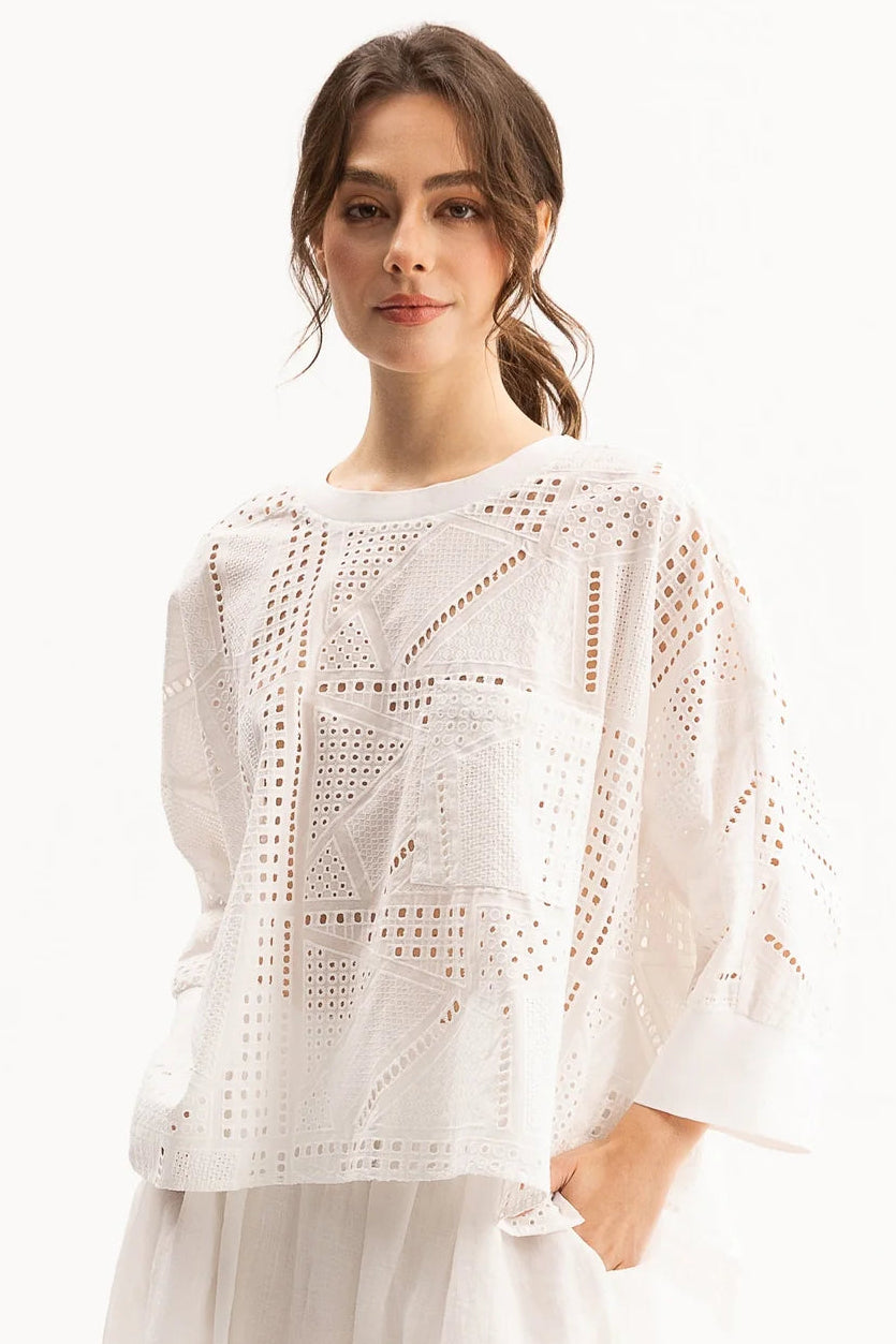 A woman wearing a white eyelet crochet top with three-quarter sleeves and a matching white skirt, photographed against a clean white studio background.