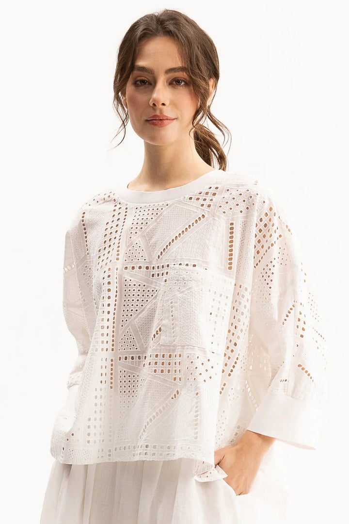 A woman wearing a white eyelet crochet top with three-quarter sleeves and a matching white skirt, photographed against a clean white studio background.