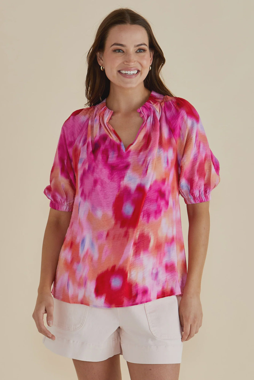 Woman wearing a pink floral betty basics blouse against a beige background