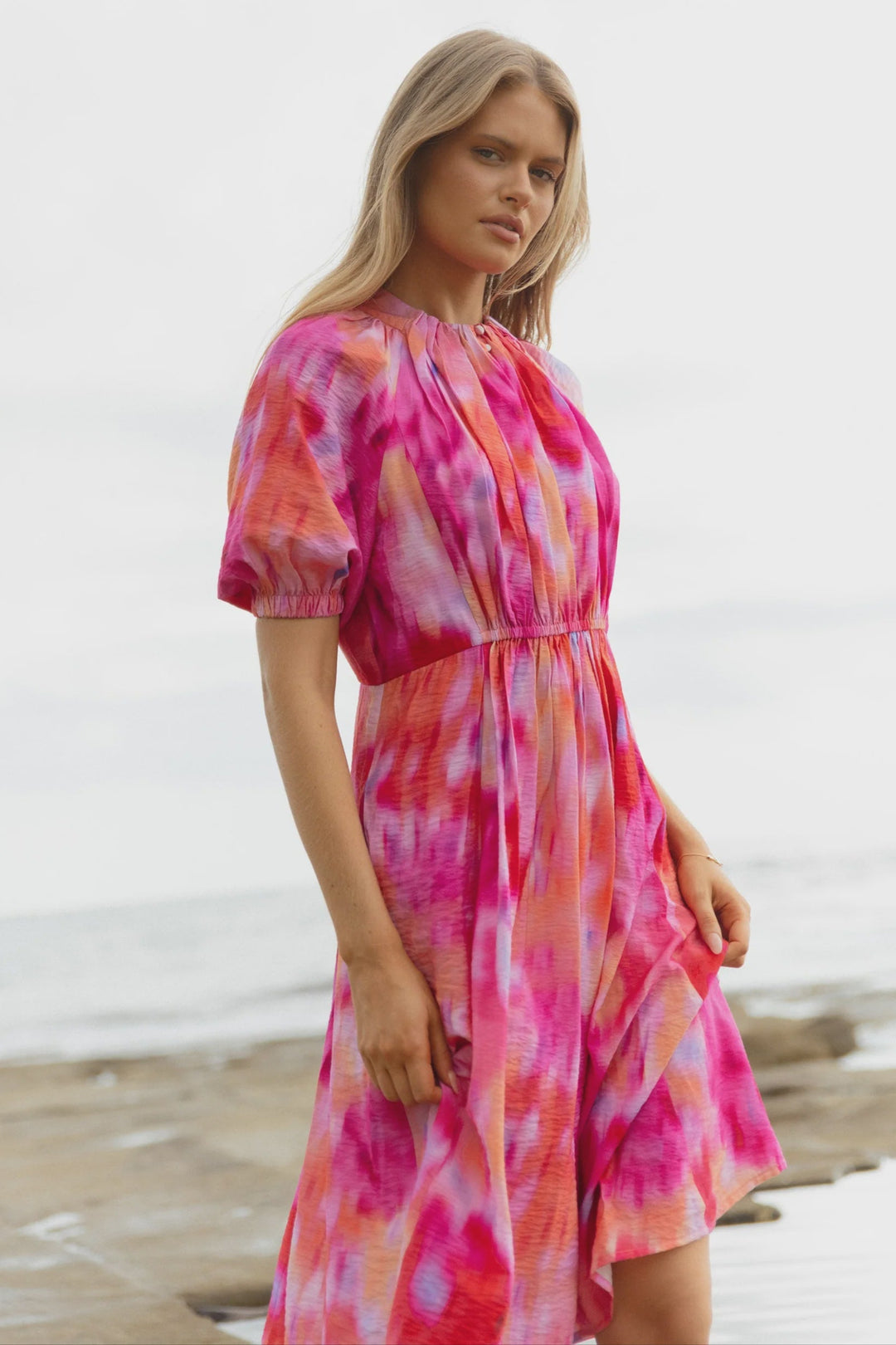 Woman wearing a pink and pink floral betty basics dress on a beach.