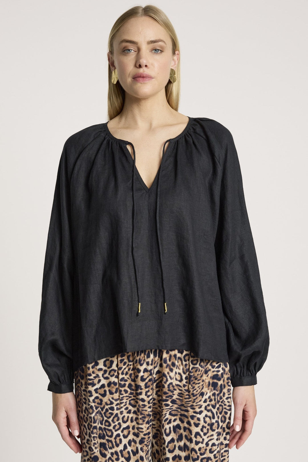 Woman wearing a black blouse and leopard print pants on a plain background