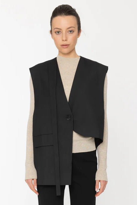 Person wearing a black vest over a beige top with black pants on a white background