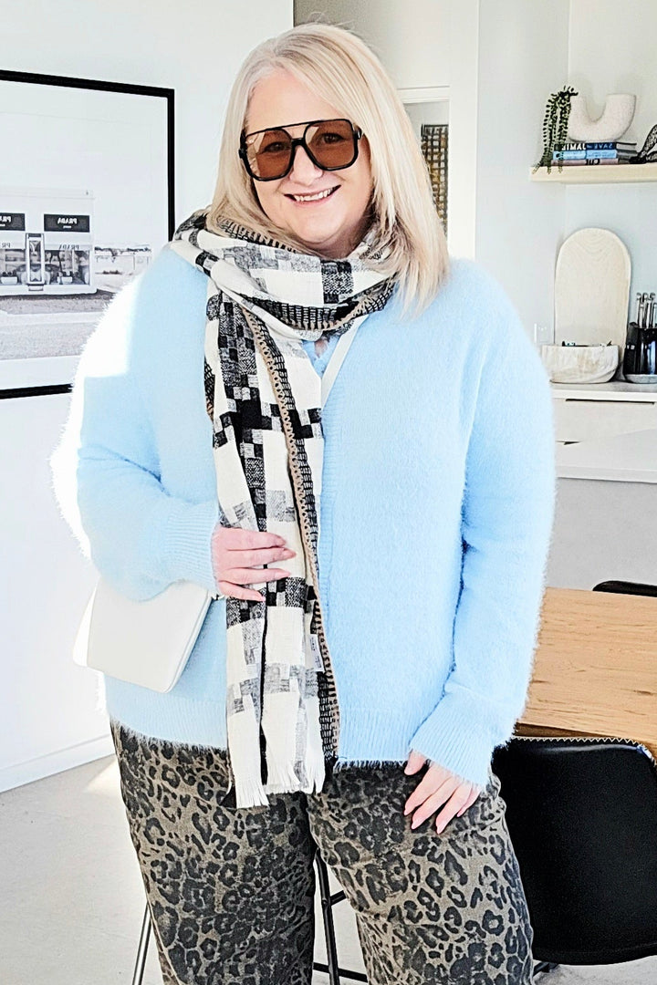 Woman standing in a modern office space wearing sunglasses and a light blue sweater.