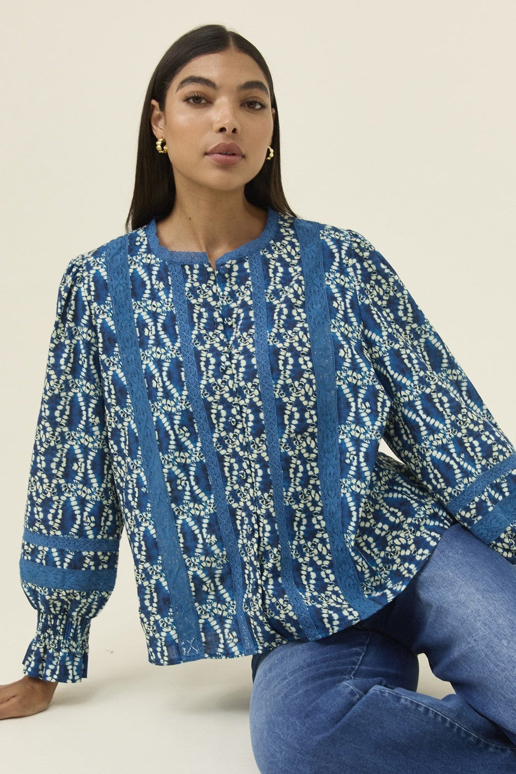 Woman wearing a blue patterned top and jeans on a beige background