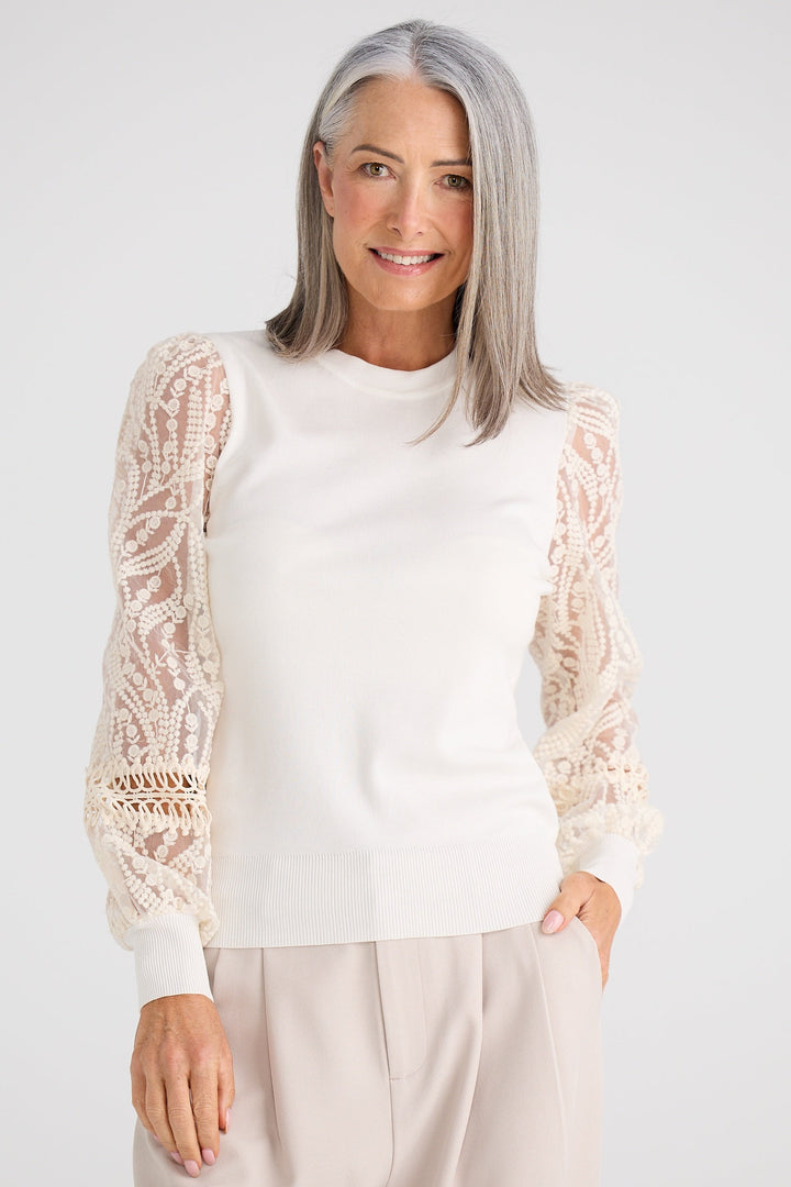 Woman wearing a white blouse with lace sleeves on a plain background