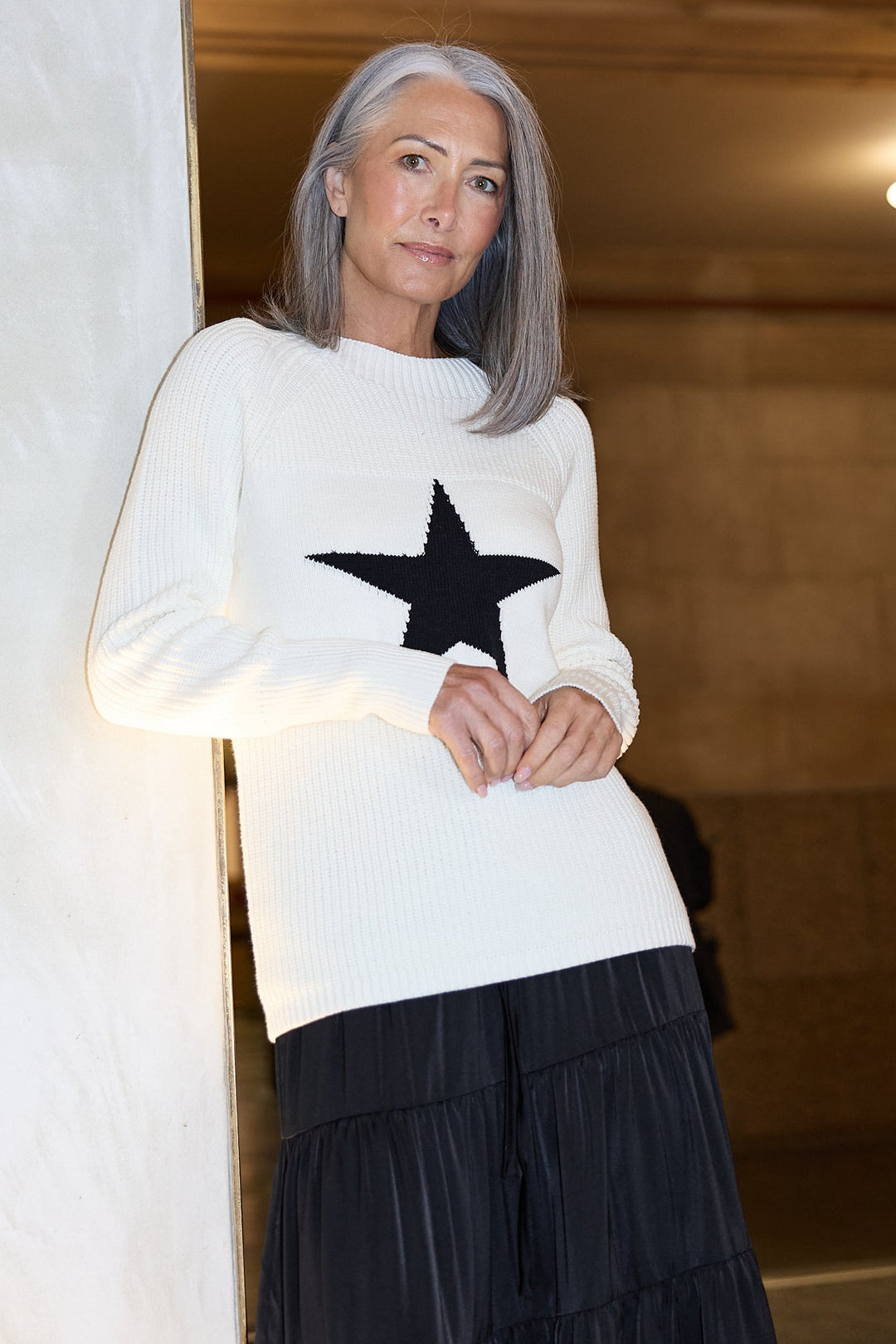 Woman wearing a white sweater with a black star design in front of a station entrance.