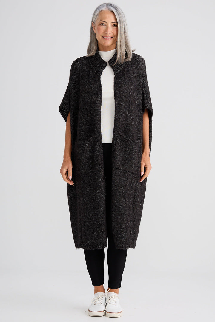 Woman wearing a long dark gray cardigan over a white shirt on a light gray background