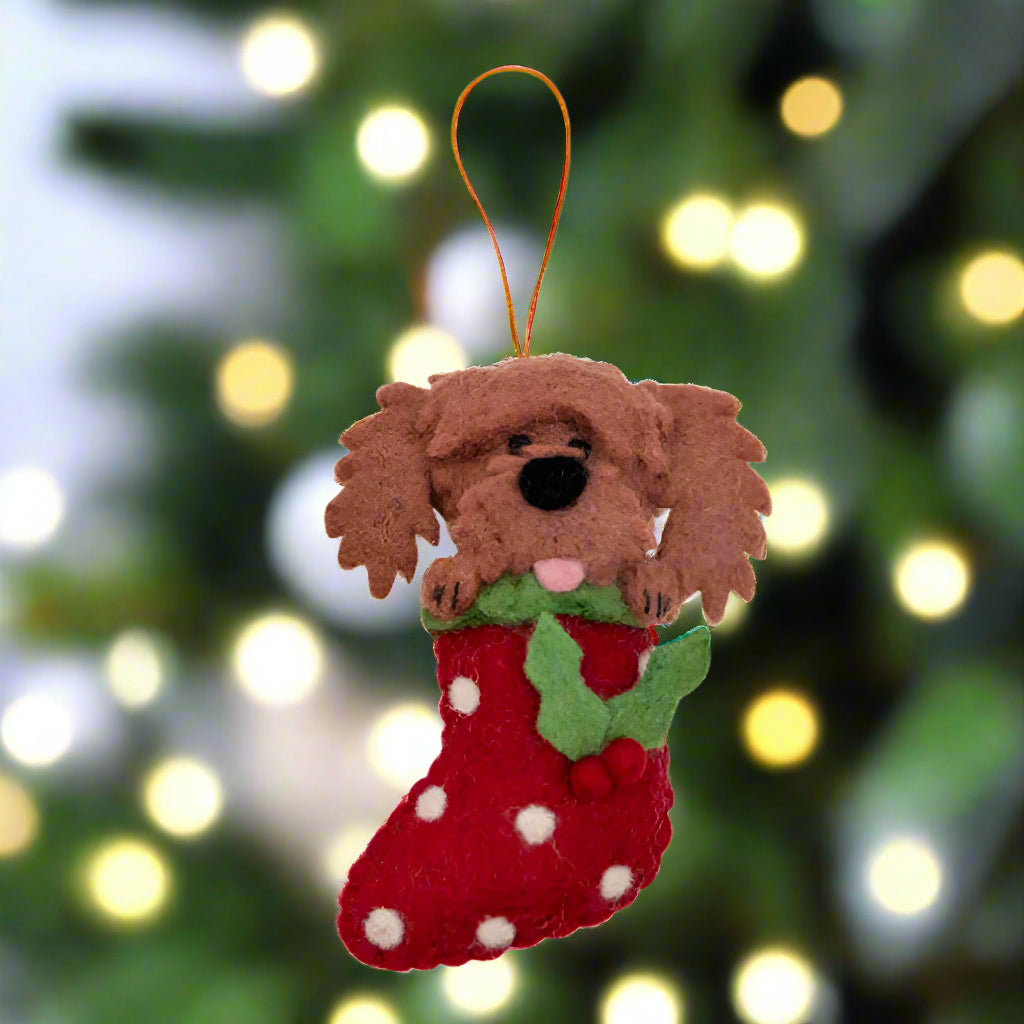 Felt dog ornament holding a red stocking with white polka dots on a white background