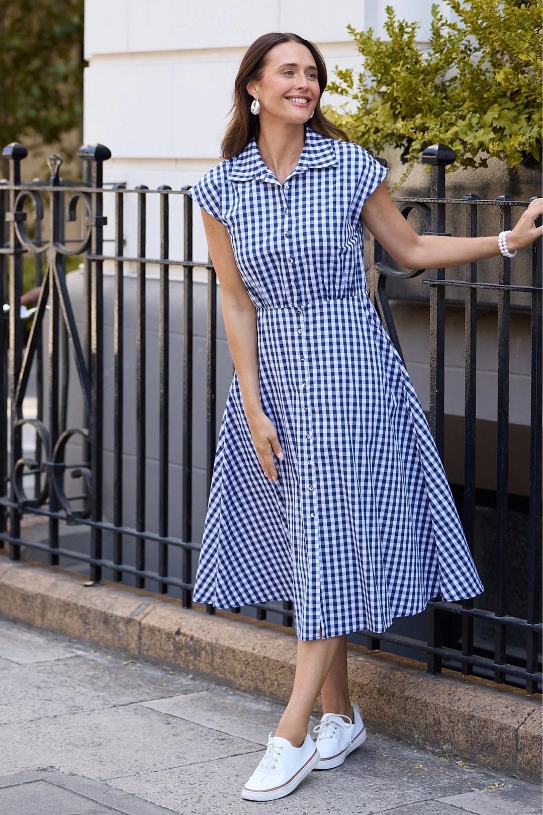 Woman in a blue brave & true checkered gingham dress standing on a sidewalk with a bicycle and building in the background
