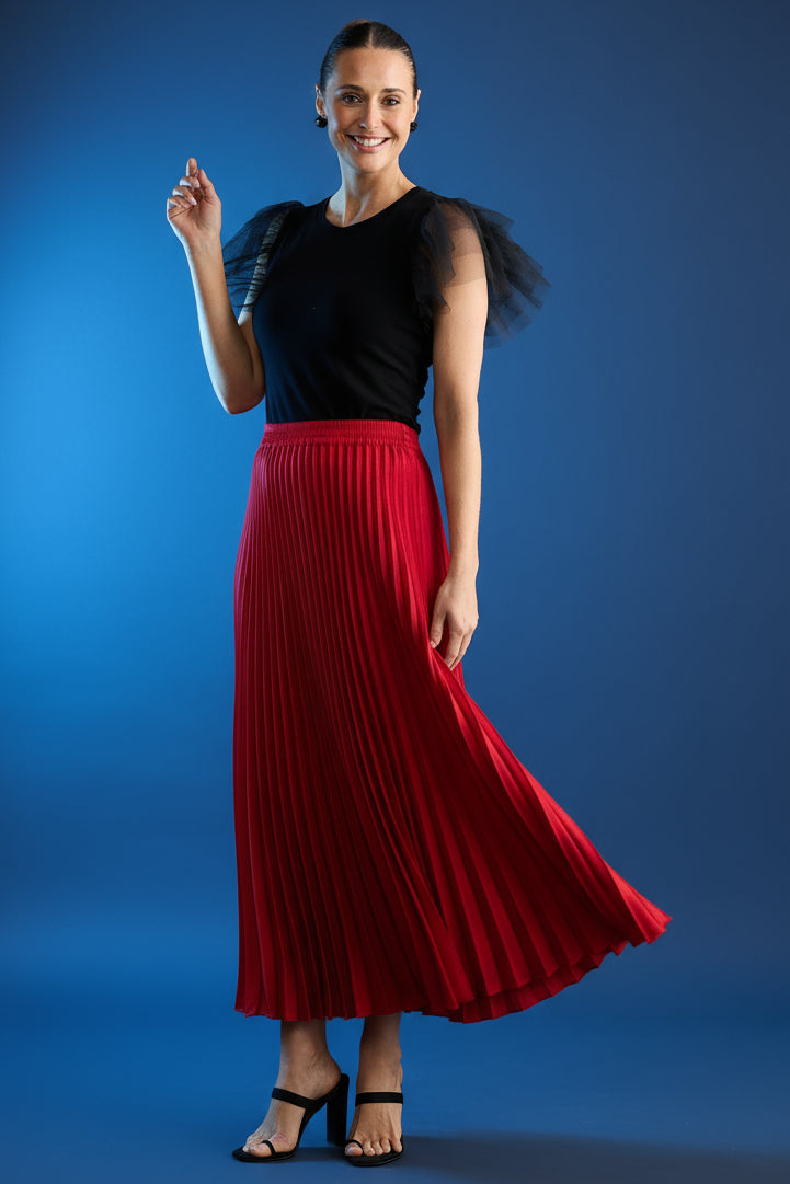 Woman wearing a black top and red pleated brave & true alias skirt against a dark background