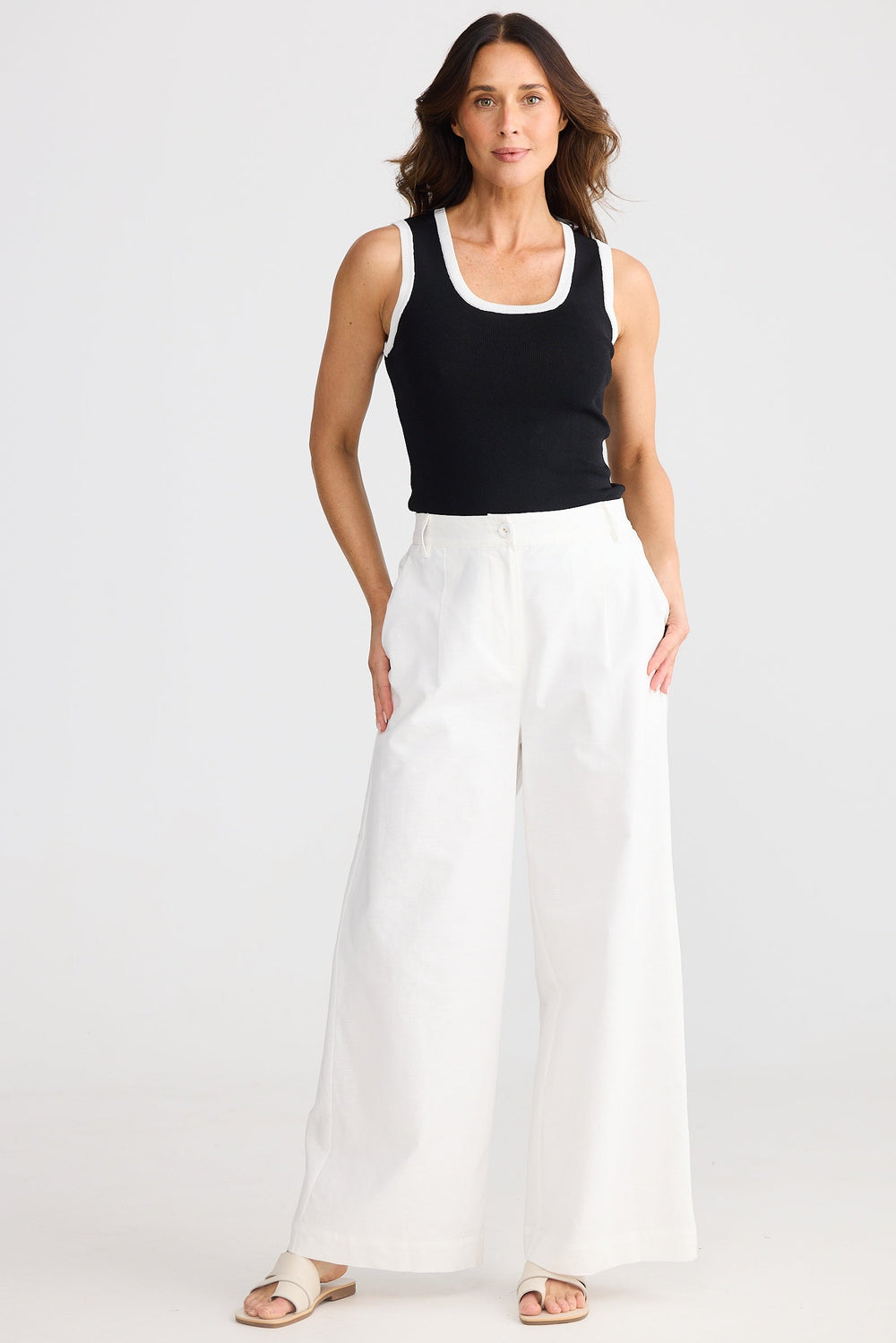 Woman wearing a black tank top and white brave & true august wide leg pants on a white background