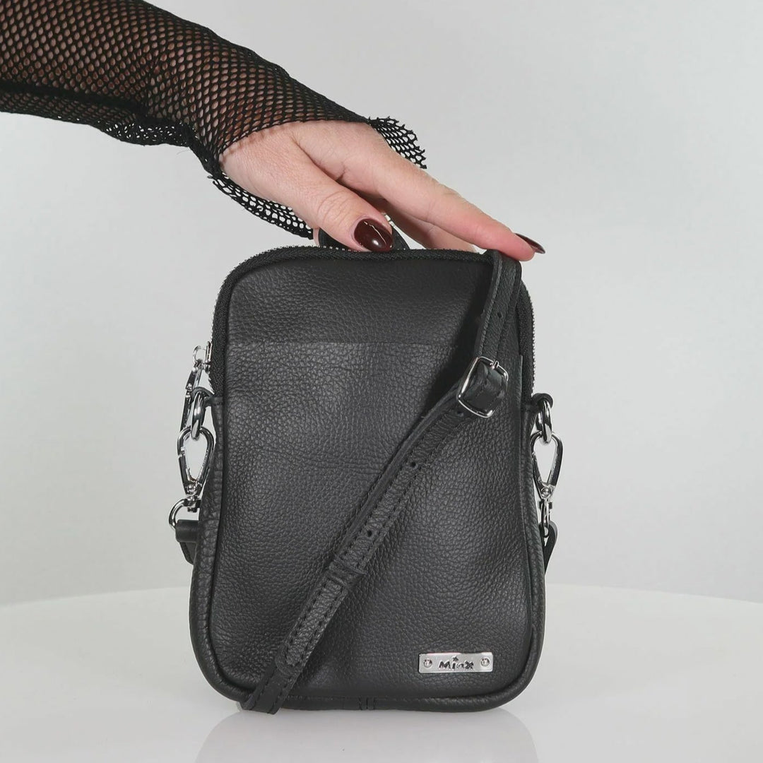 Black leather crossbody bag held by a hand on a white background