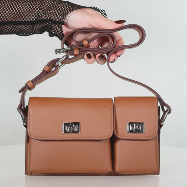 Brown leather handbag with a strap held by a hand on a white background