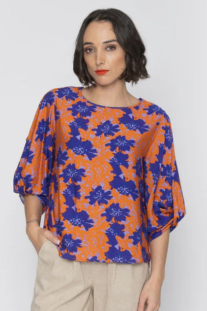 Woman wearing a colorful floral blouse and beige shorts on a white background