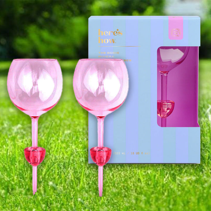 Two pink wine glasses that have stems that can stab into grass or sand perfect for picnics and a packaging box on grass.